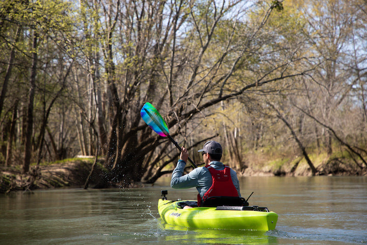 man kayaks on a river surrounded by trees