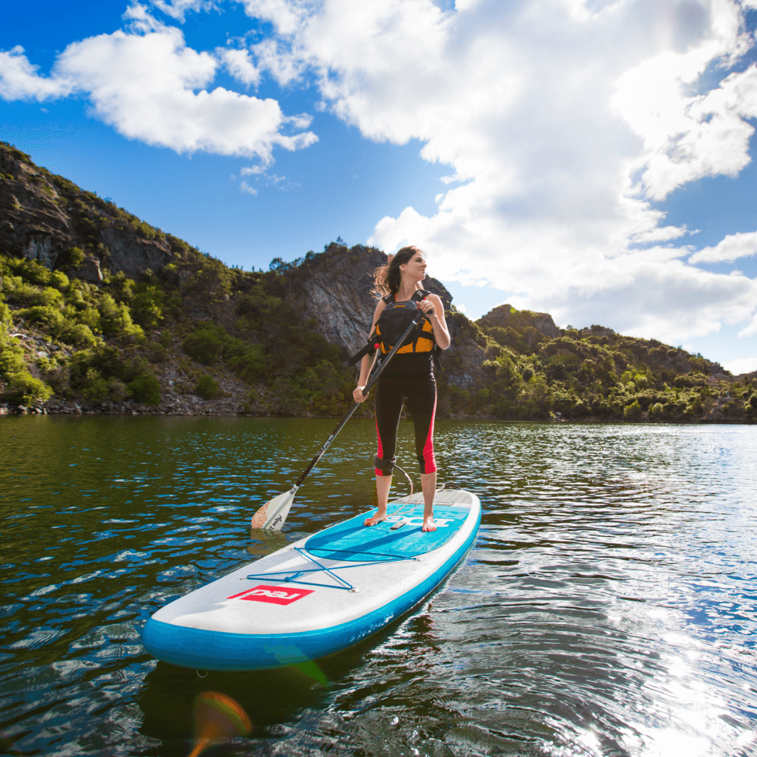 girl on paddle board with grassy mountains behind her using the Lyric 2-piece SUP paddle