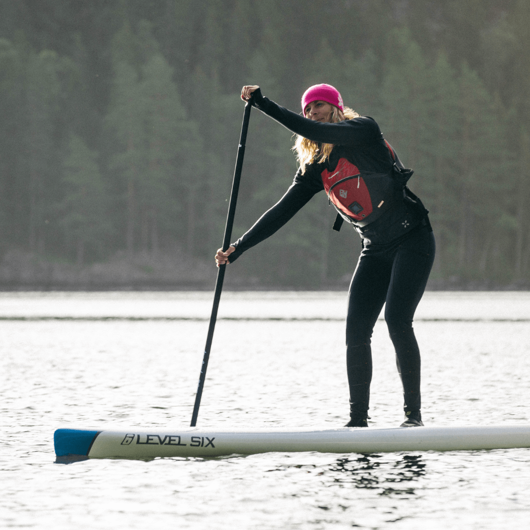 Woman in pink winter hat paddling Level Six paddle board with berry SUP paddle#color_berry