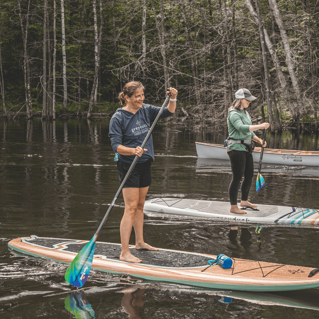 woman paddling with 2-piece northern lights SUP paddle on Grey Duck paddle board#color_northern-lights