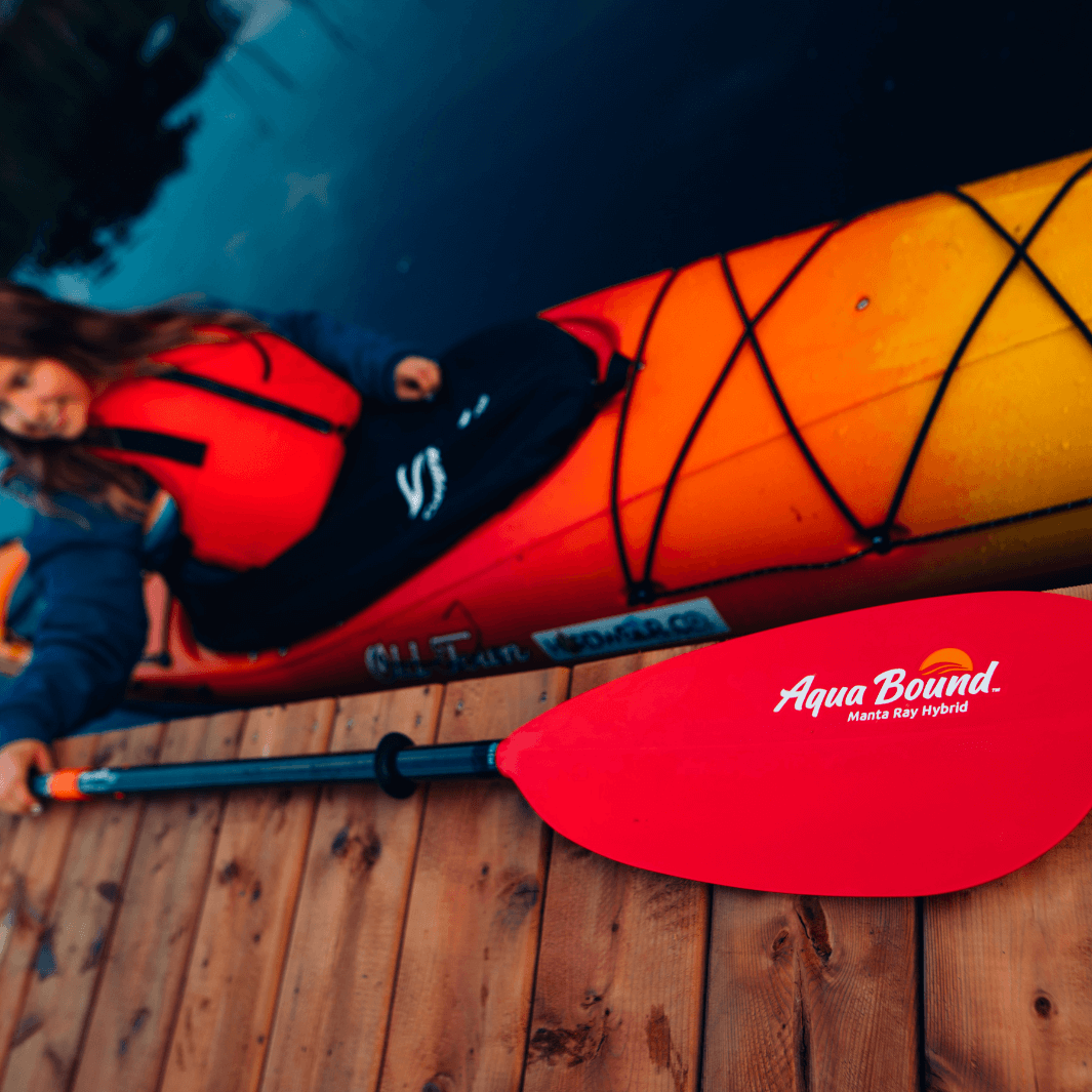 manta ray hybrid 2-piece posi-lok sunset red laying on dock with girl in kayak reaching up to grab it#color_sunset-red