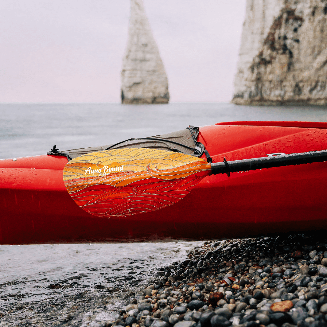 whiskey fuego paddle on side of red sea kayak positioned on pebble beach#color_fuego